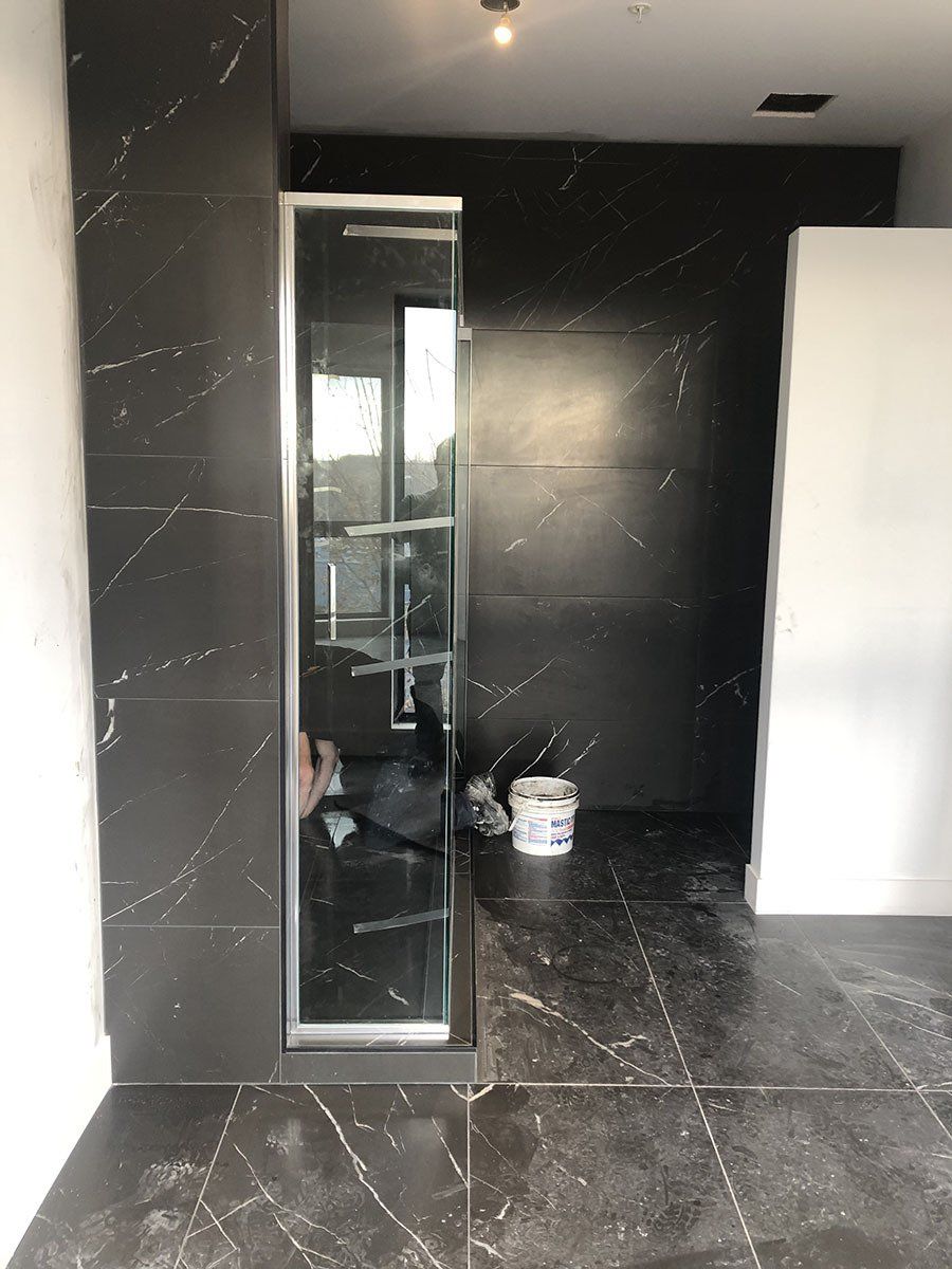 Bathroom with black marble tile walls and floor. Glass shower enclosure is installed.
