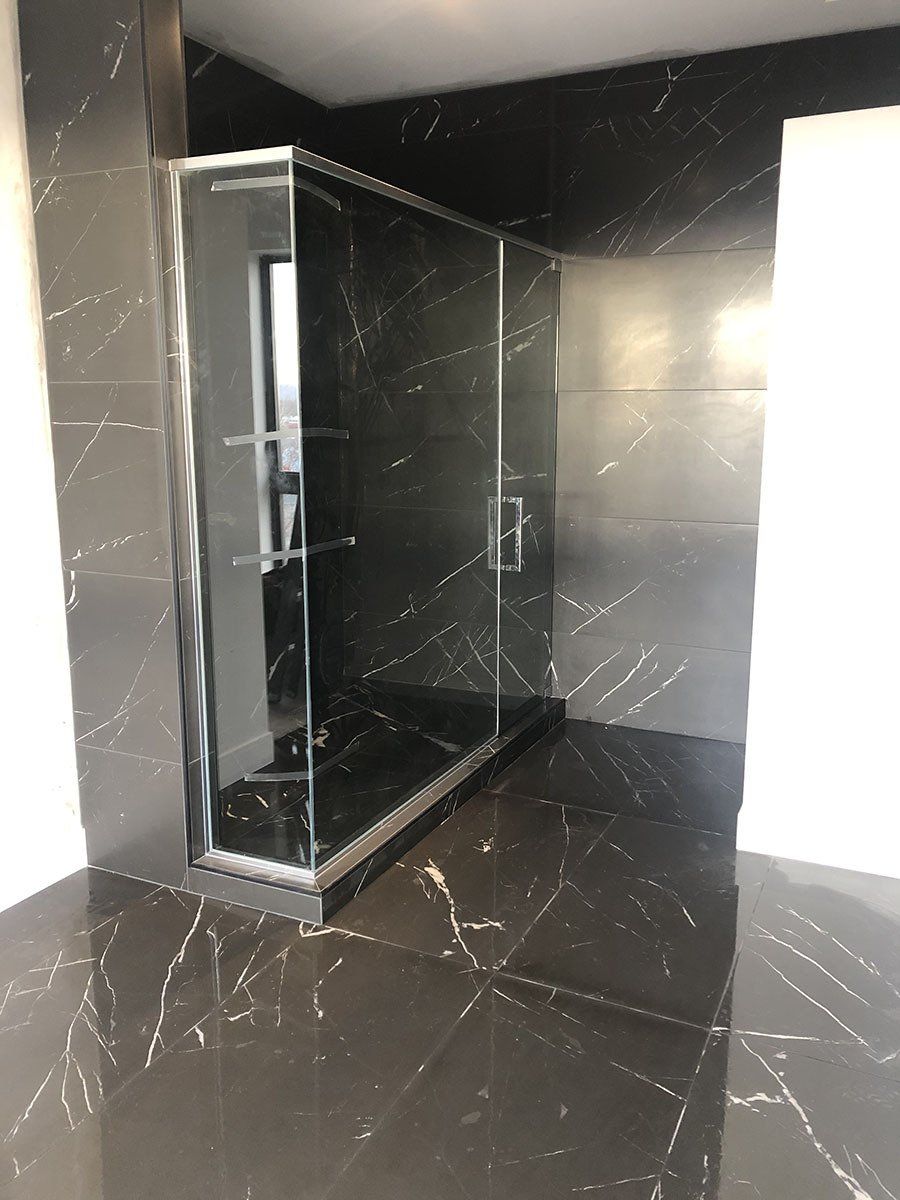 Salle de bains en marbre noir avec cabine de douche en verre.