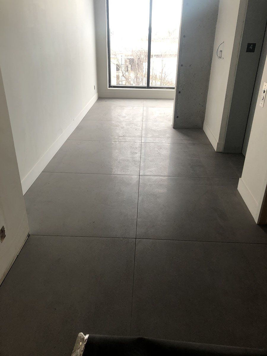 Gray flooring in an empty room, with a window at the end and white walls.