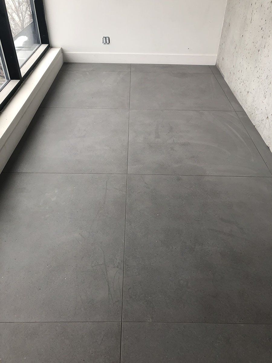 Gray tiled floor in an empty room, next to a window and white wall.