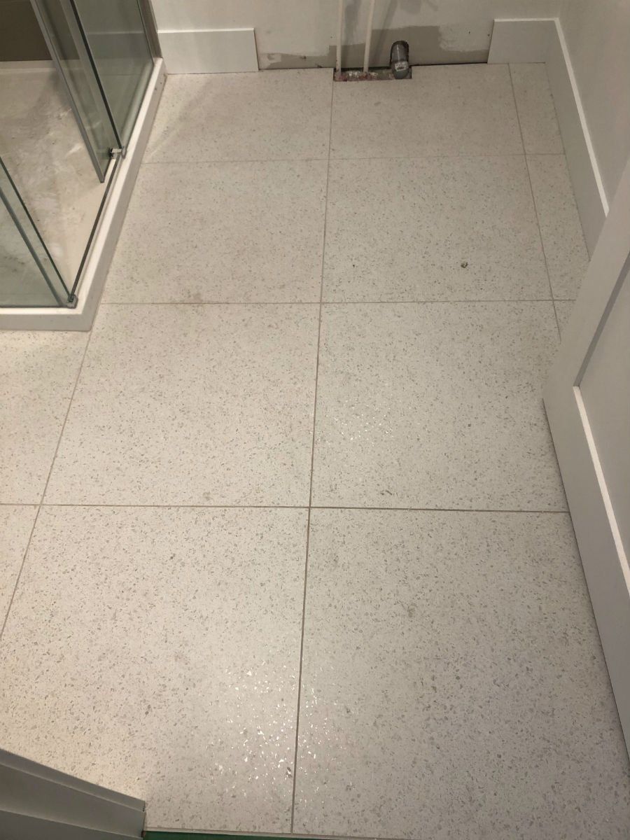 White speckled tile floor in a bathroom, with a shower and door frame visible.