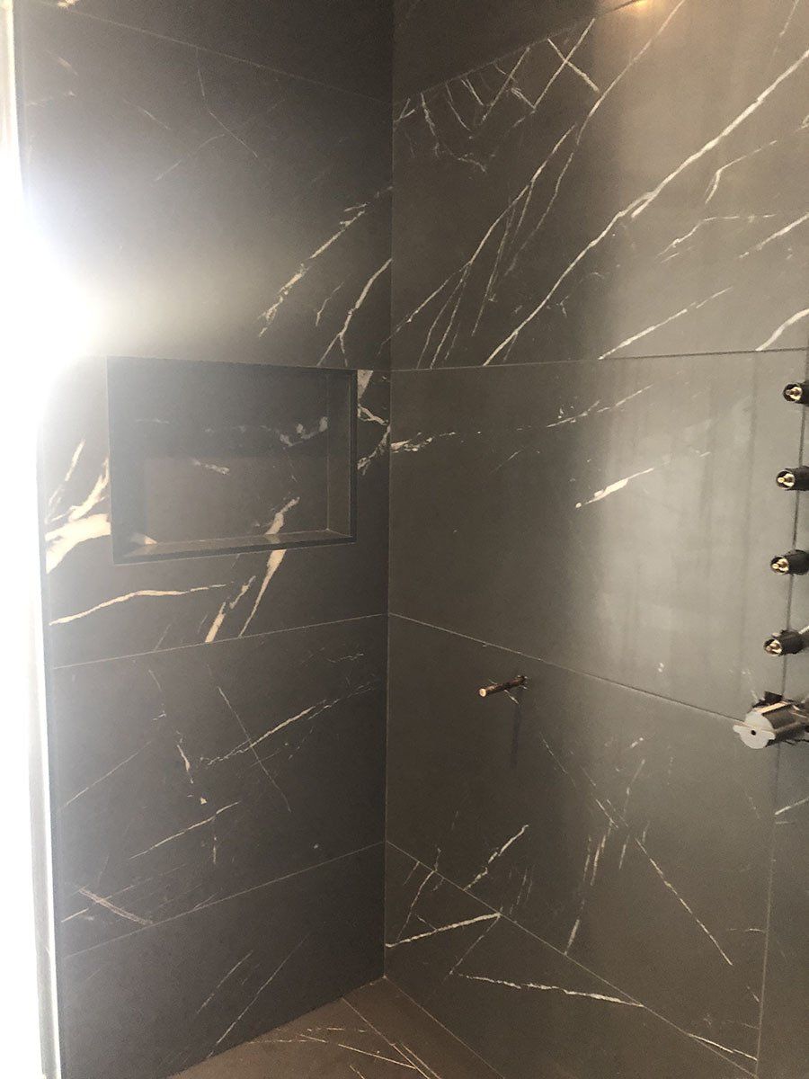 Dark shower with marble-like tiles, built-in shelf, and silver fixtures.