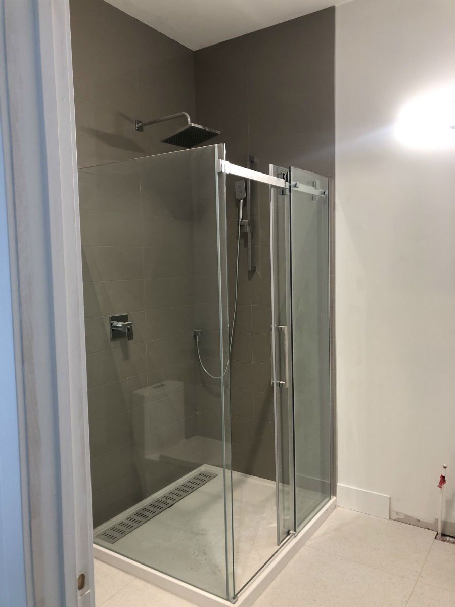 Corner shower with glass doors, silver fixtures, and grey walls.