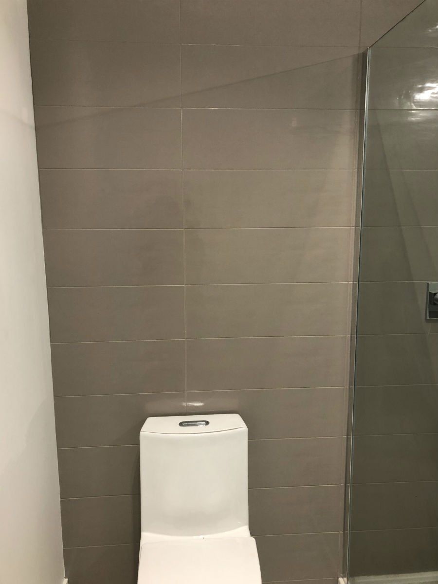 Toilet against gray tiled wall, beside glass shower door.