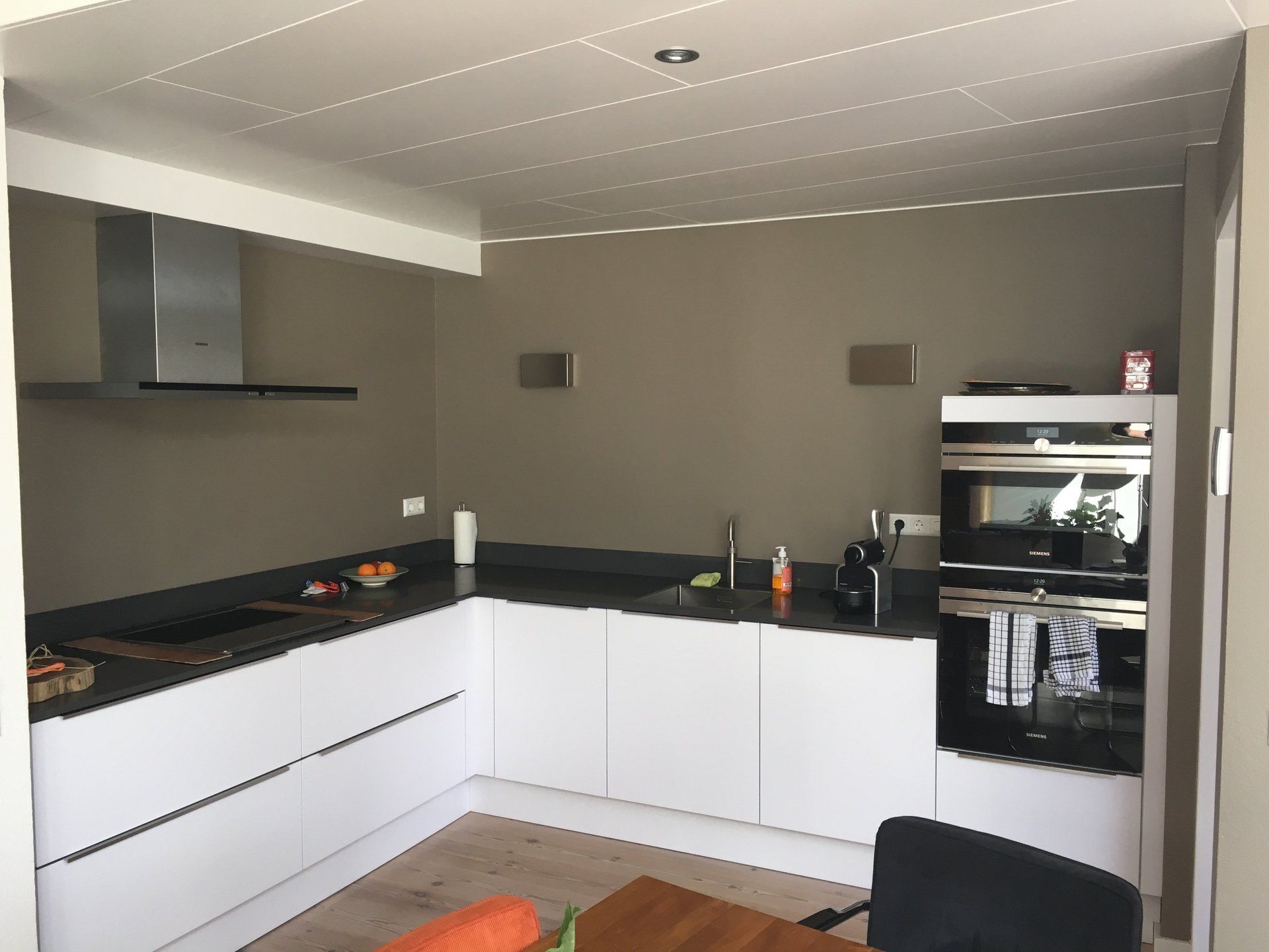 Moderne keuken met witte kasten, zwarte werkbladen en een ingebouwde oven onder een schuin plafond.