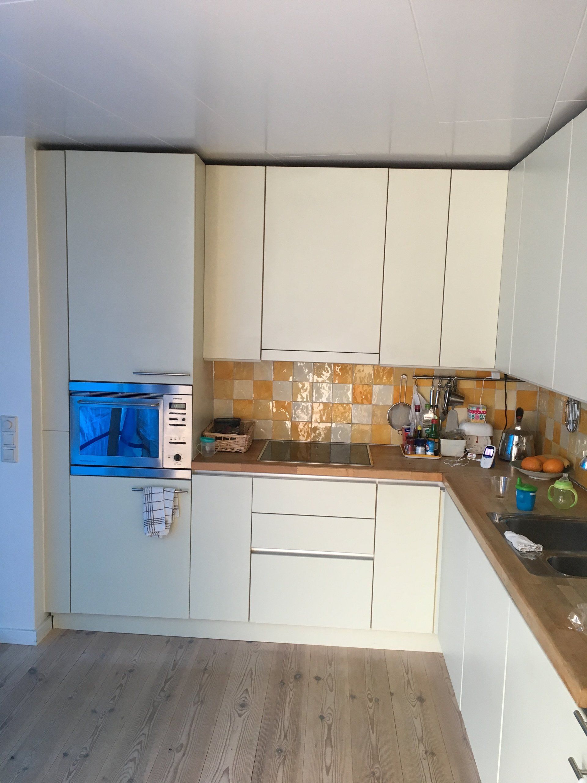 Moderne keuken met witte kasten, houten aanrechtbladen, betegelde achterwand en een inbouwapparatuurnis met blauwe verlichting.