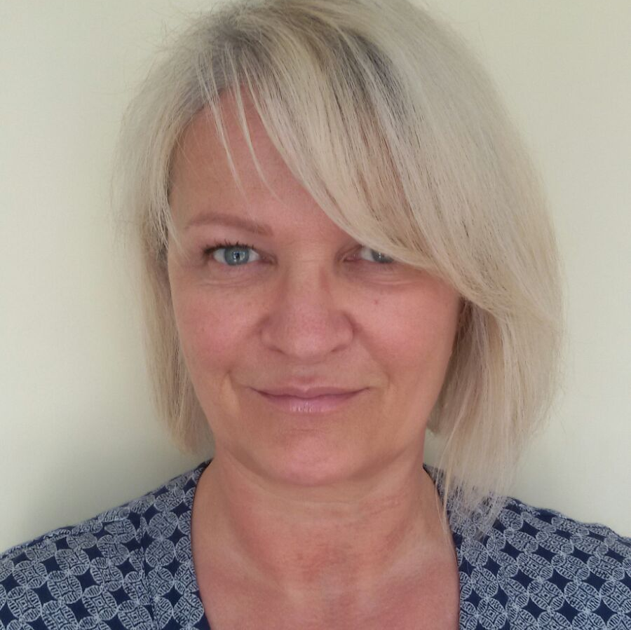 Eine Frau mit blonden Haaren und blauen Augen lächelt in die Kamera.