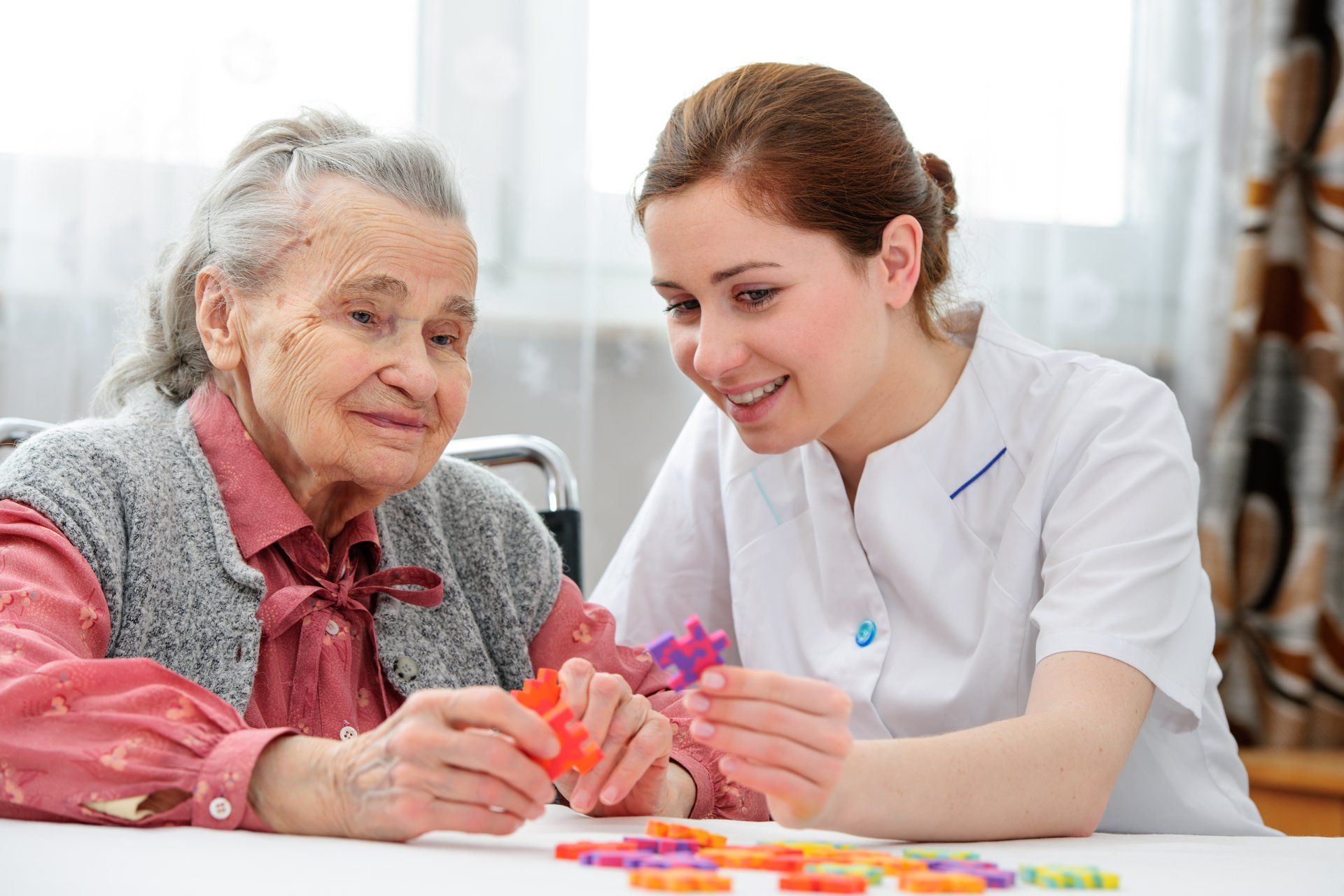 A nurse is helping an elderly woman with a puzzle.