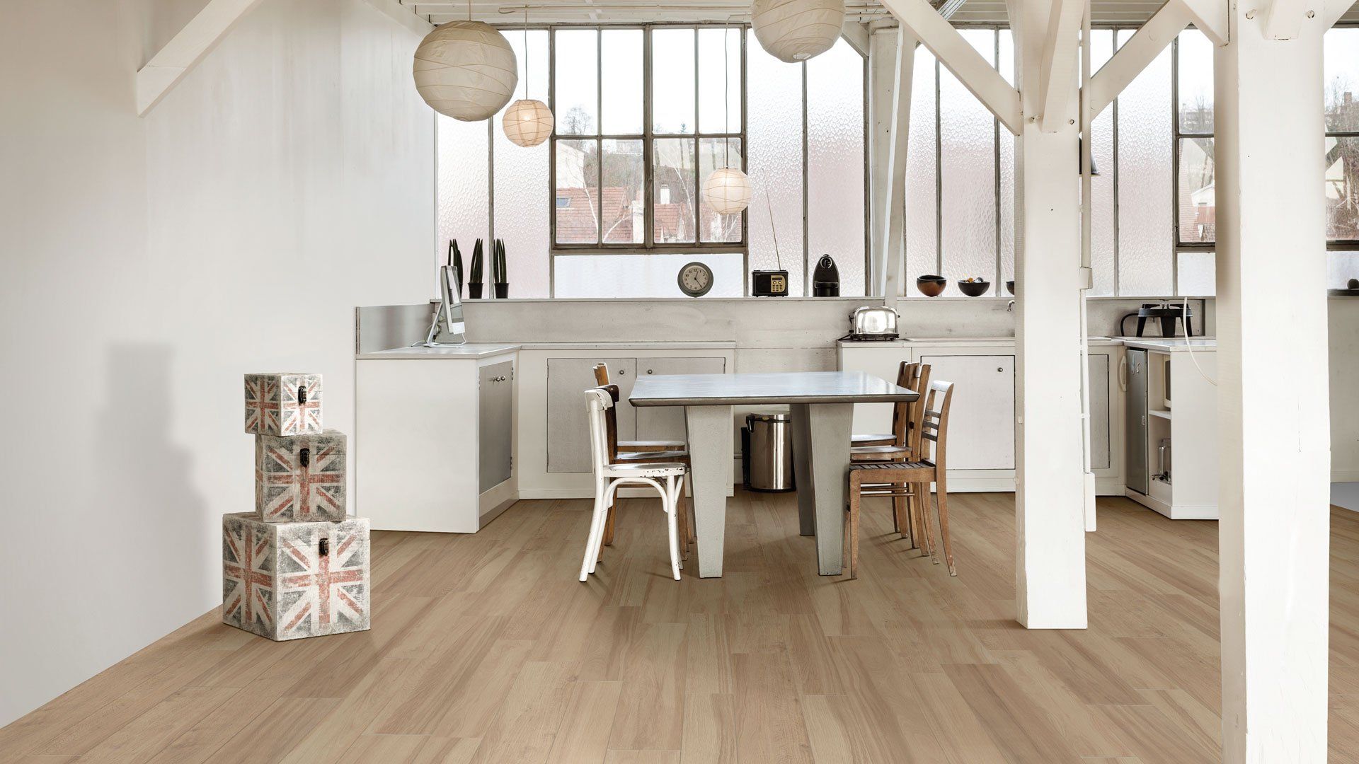 Sala da pranzo luminosa e ariosa con tavolo e sedie in legno, travi bianche e ampie finestre.