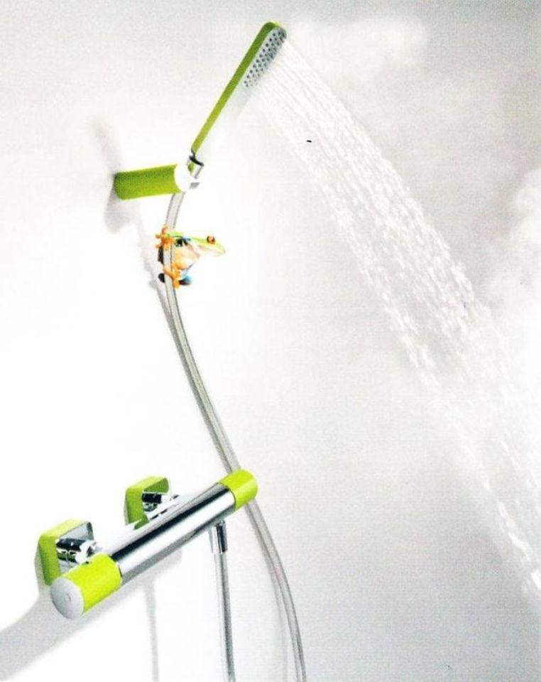 Soffione doccia verde e bianco che spruzza acqua su una parete bianca del bagno.