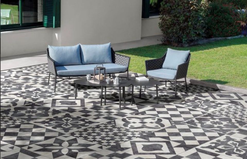 Zona relax all'aperto con divanetto blu, sedie e tavolo rotondo su una terrazza con motivo a righe bianche e nere.