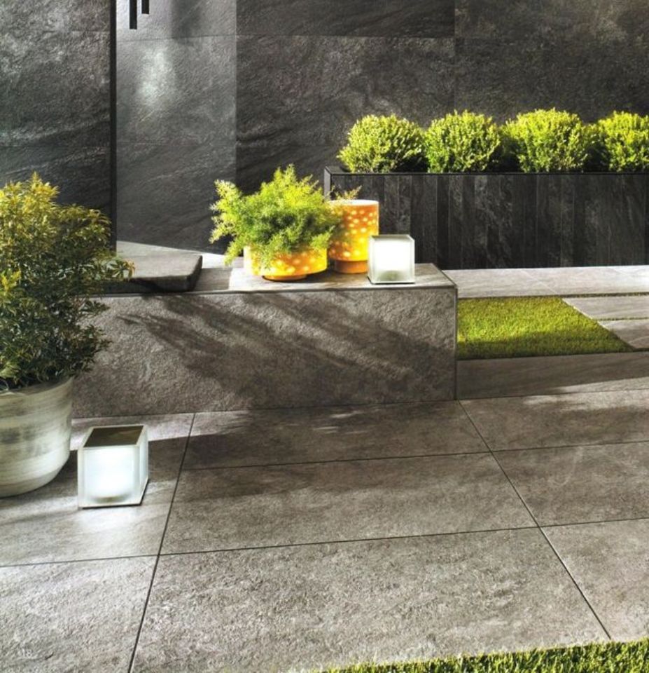 Patio moderno con scalini in pietra, piante verdi in vaso e luci da esterno che illuminano il crepuscolo.