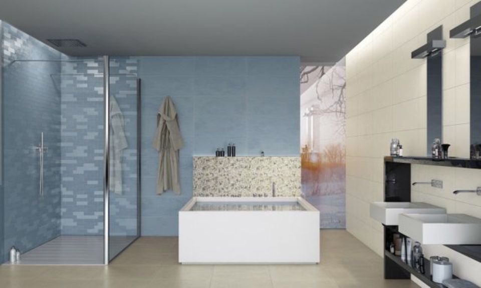 Bagno moderno con doccia in vetro blu, vasca freestanding e pareti rivestite con piastrelle beige.