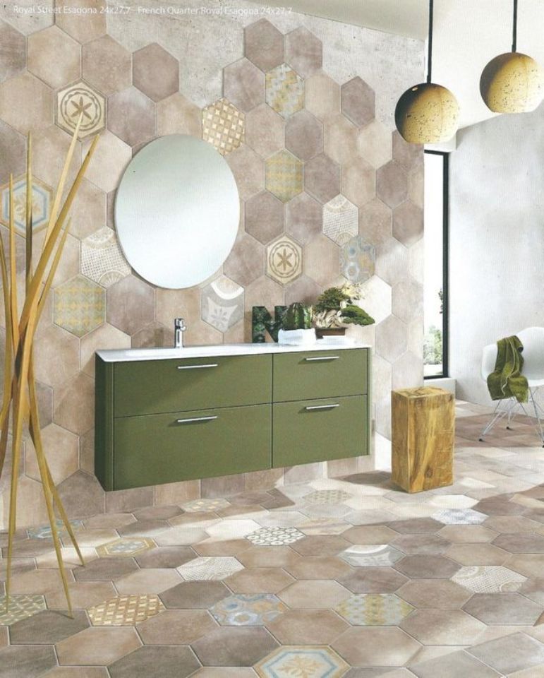 Bagno moderno con pareti e pavimento rivestiti con piastrelle esagonali, mobile lavabo verde, specchio rotondo e lampade a sospensione.