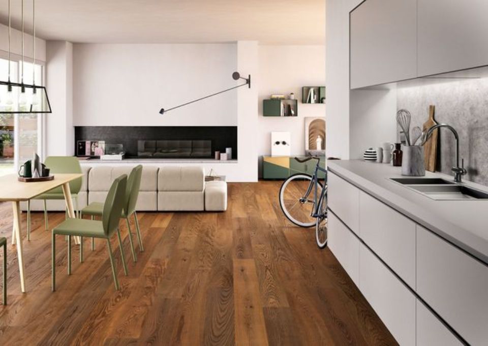 Cucina e soggiorno moderni a pianta aperta con pavimento in legno, mobili bianchi, sedie verdi e una bicicletta nelle vicinanze.