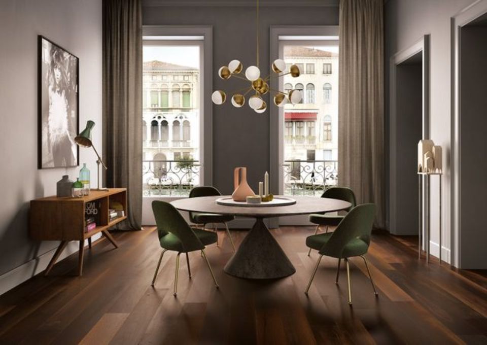 Sala da pranzo moderna con tavolo rotondo, sedie verdi e ampie finestre che si affacciano su una strada cittadina.