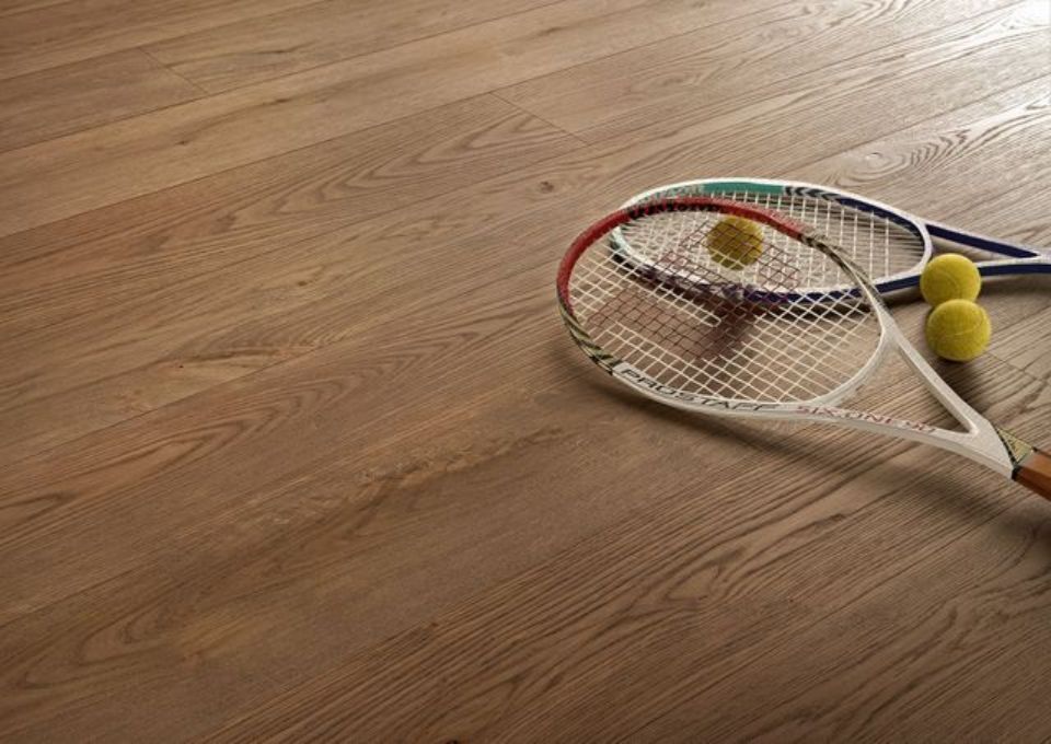 Racchetta da tennis e due palline da tennis gialle su un pavimento di legno.
