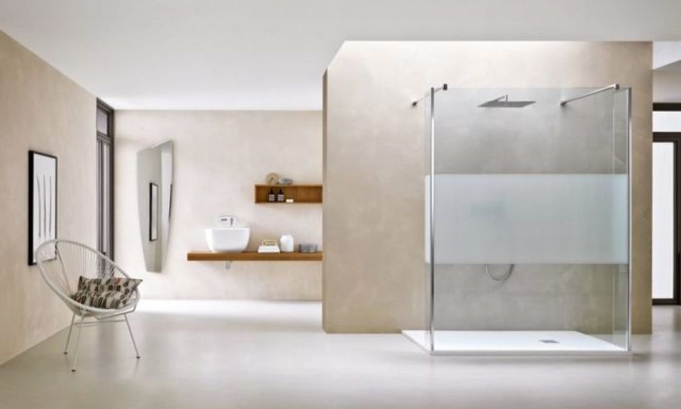 Bagno minimalista con doccia in vetro, vasca bianca e mensole sospese in un ambiente interno beige.