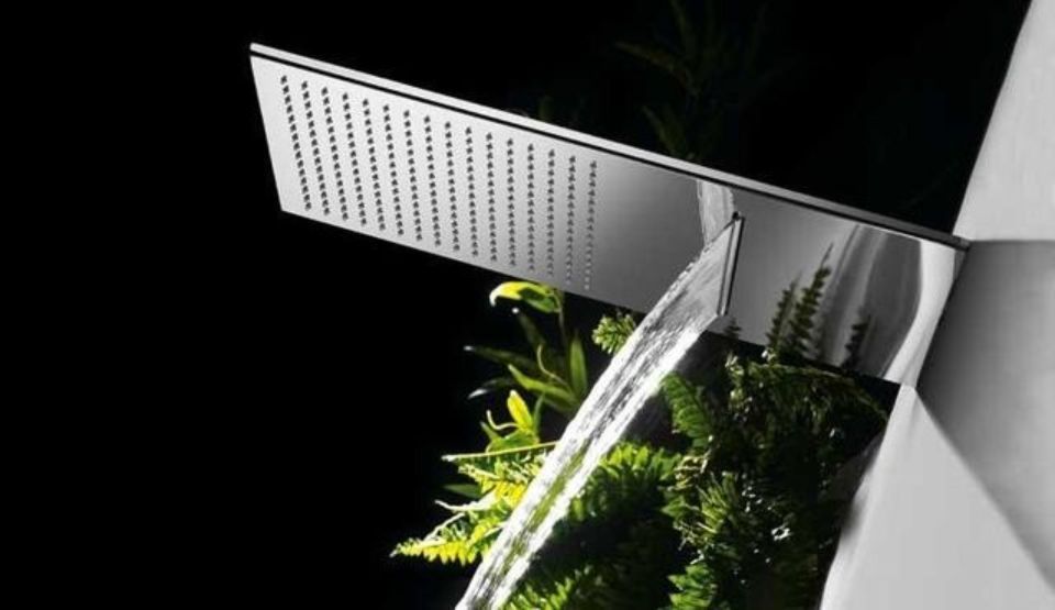 Doccia esterna moderna con pannello cromato e getto d'acqua che di notte si riversa su piante verdi.