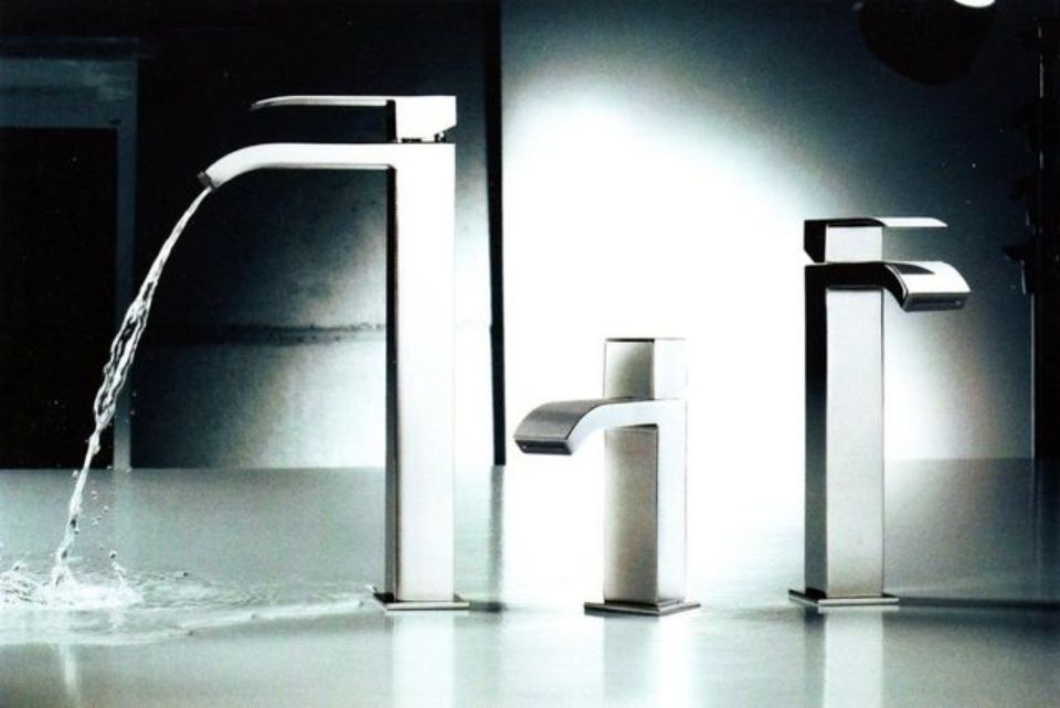 Tre moderni rubinetti cromati su una superficie riflettente, uno dei quali eroga acqua, su uno sfondo scuro.