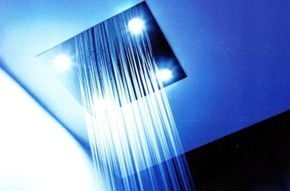 Soffione doccia a soffitto che spruzza acqua in un bagno illuminato di blu