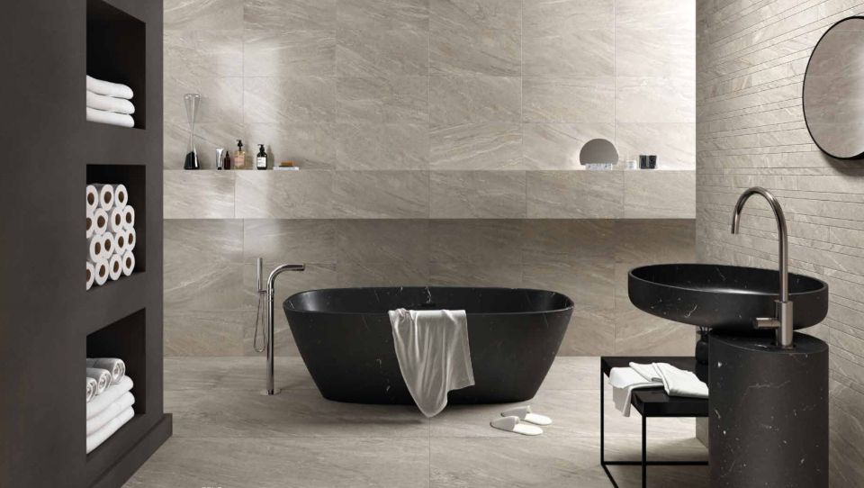 Bagno minimalista con due vasche da bagno nere, pareti in pietra, mensole e uno specchio rotondo.