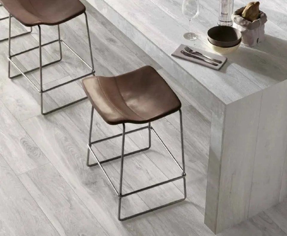 Due sgabelli marroni accanto a un tavolo di legno chiaro su un pavimento grigio chiaro.