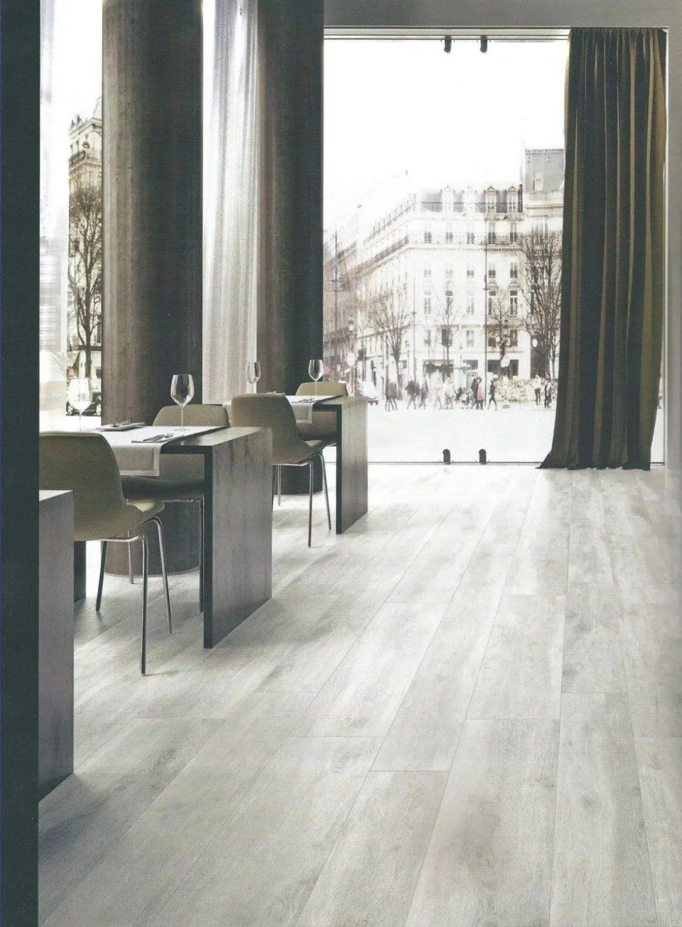 Interno minimalista del caffè con alte colonne, tavoli e una luminosa vista sulla strada attraverso ampie vetrate.