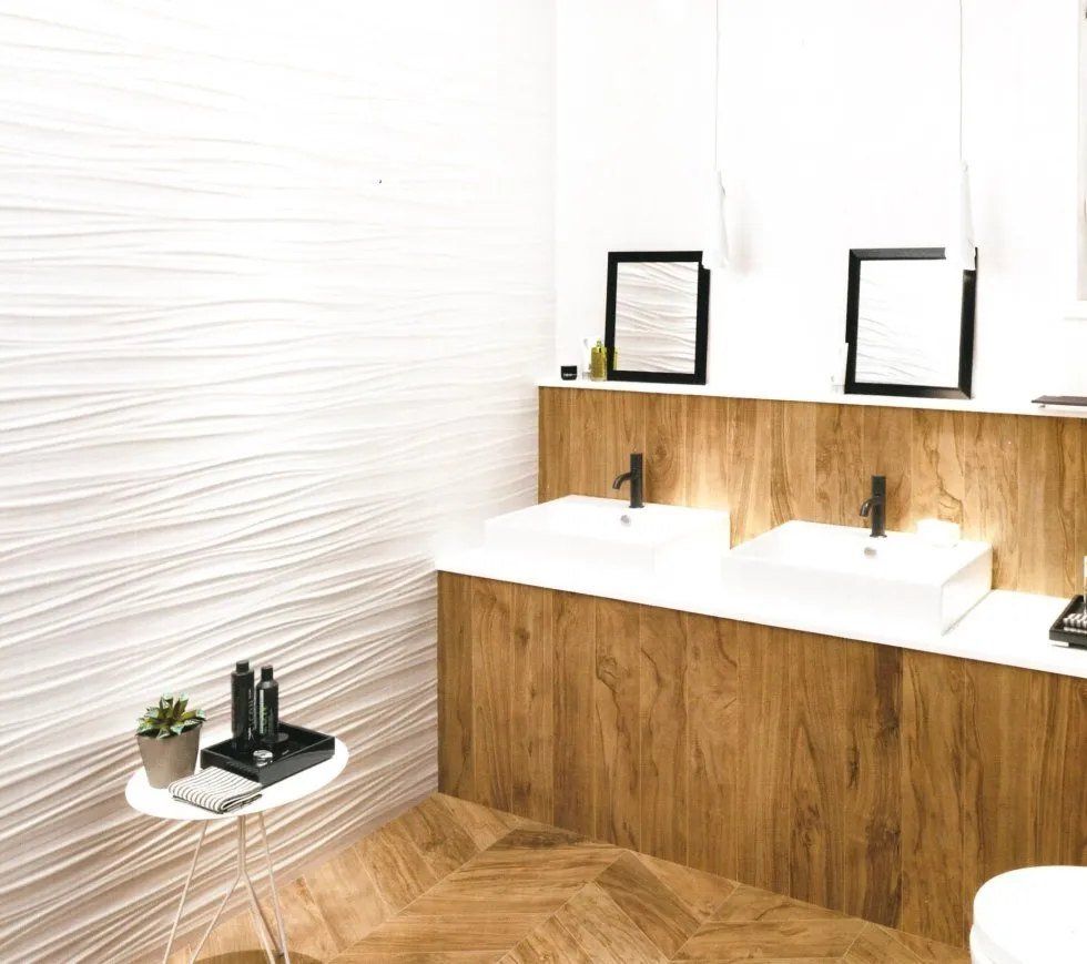Bagno luminoso e bianco con due lavandini, mobiletto in legno, specchi neri e un piccolo tavolino con articoli da toeletta e una pianta.