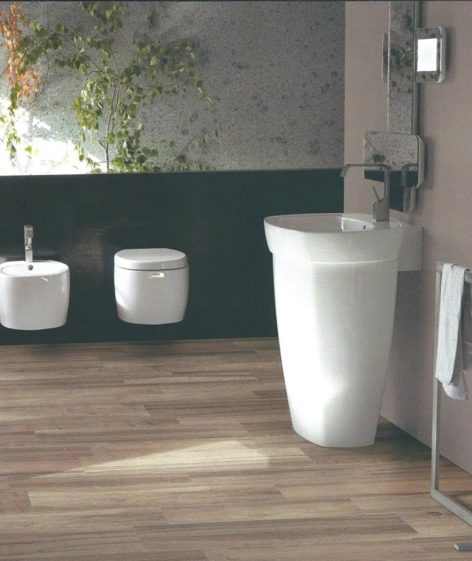 Bagno moderno con pavimento in legno, lavabo bianco, WC sospeso e portasciugamani sulla destra.