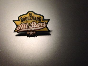 “De Boulevard All Stars” logo in black, gold, and orange on a light wall, with a spotlight effect.
