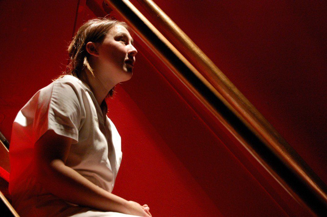 Person in a white shirt beside a red staircase, lit by warm red light.
