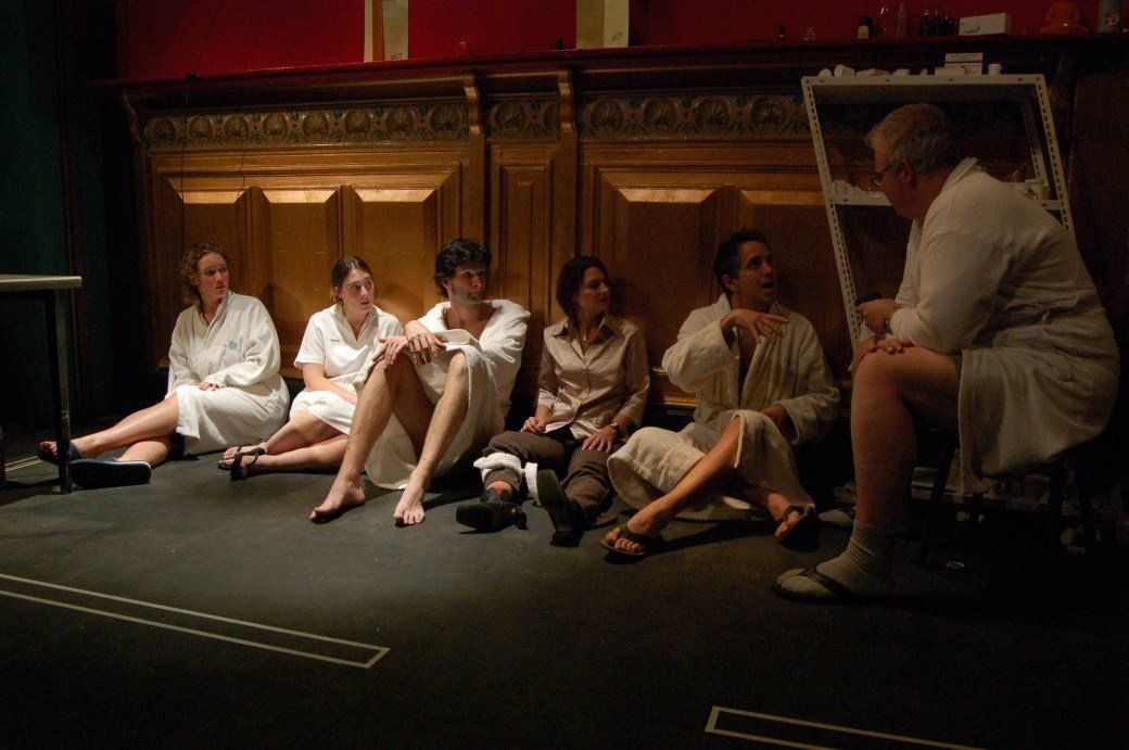 People sitting on a stage in front of wooden doors, chatting in a dimly lit theater setting