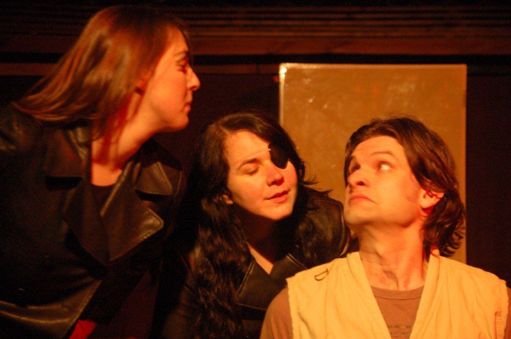 Three people in dim warm light, two looking at the person seated on the right.