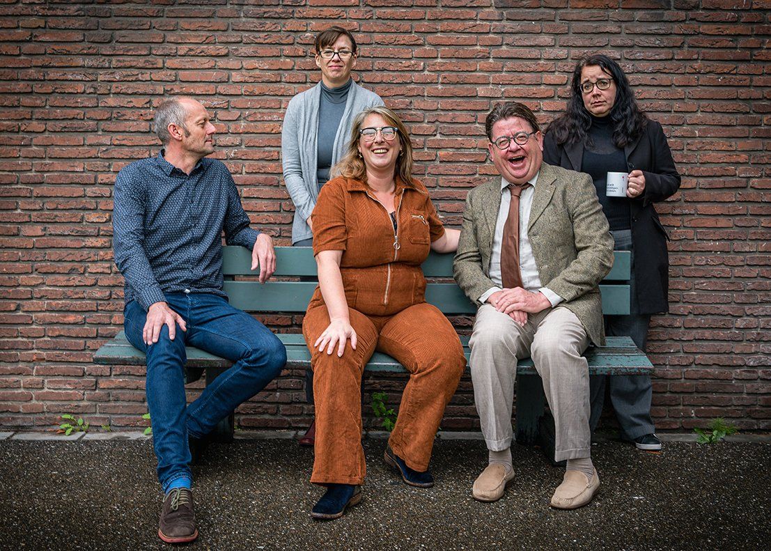 Five people posing on steps against a brick wall, wearing casual and business-casual clothes.