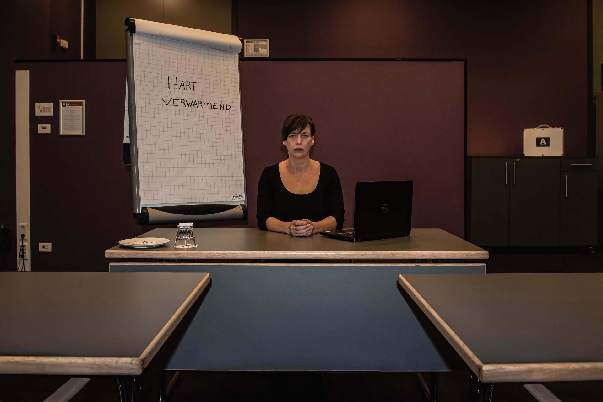 Woman seated at a front table in a classroom, beside a flip chart and laptop.
