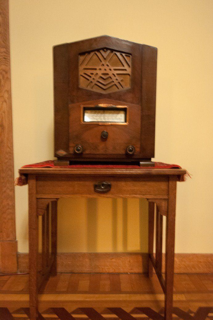 Vintage wooden radio on a small table against a yellow wall.