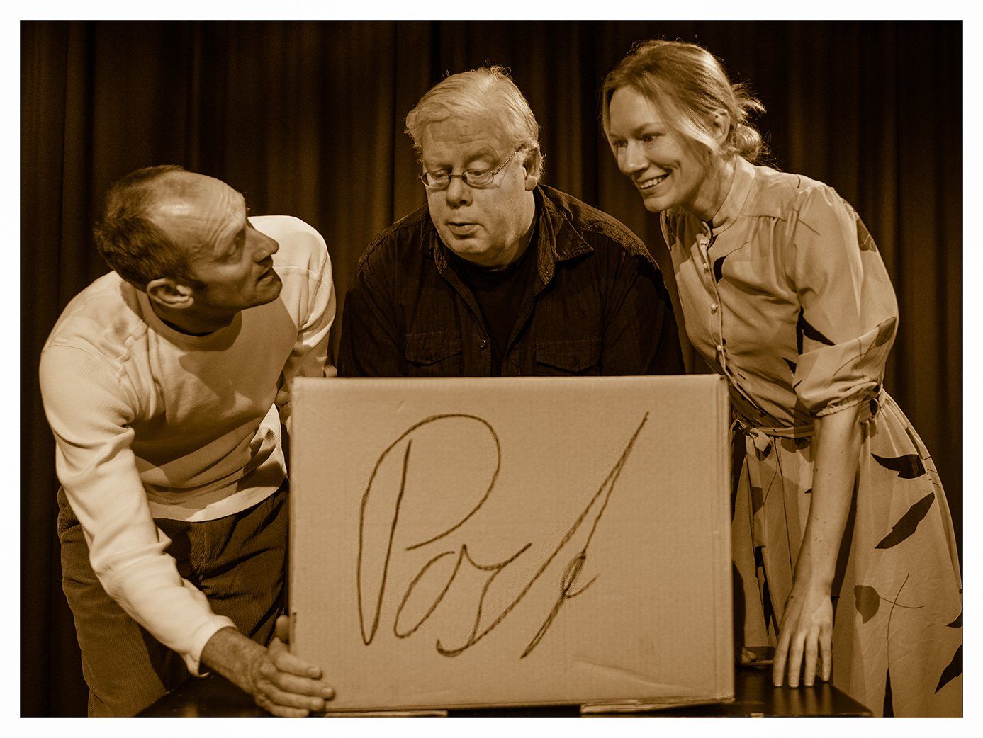 Three people smiling around a box with the word “Poof” written on it, on a stage-like backdrop.