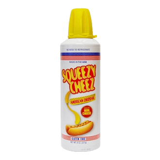 A white can of Squeezy Cheez American Cheddar cheese with a yellow cap and a graphic of cheese being squeezed on a hot dog.