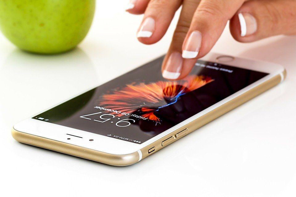 Hand with French-tipped nails touches a smartphone screen, a green apple sits in the background.