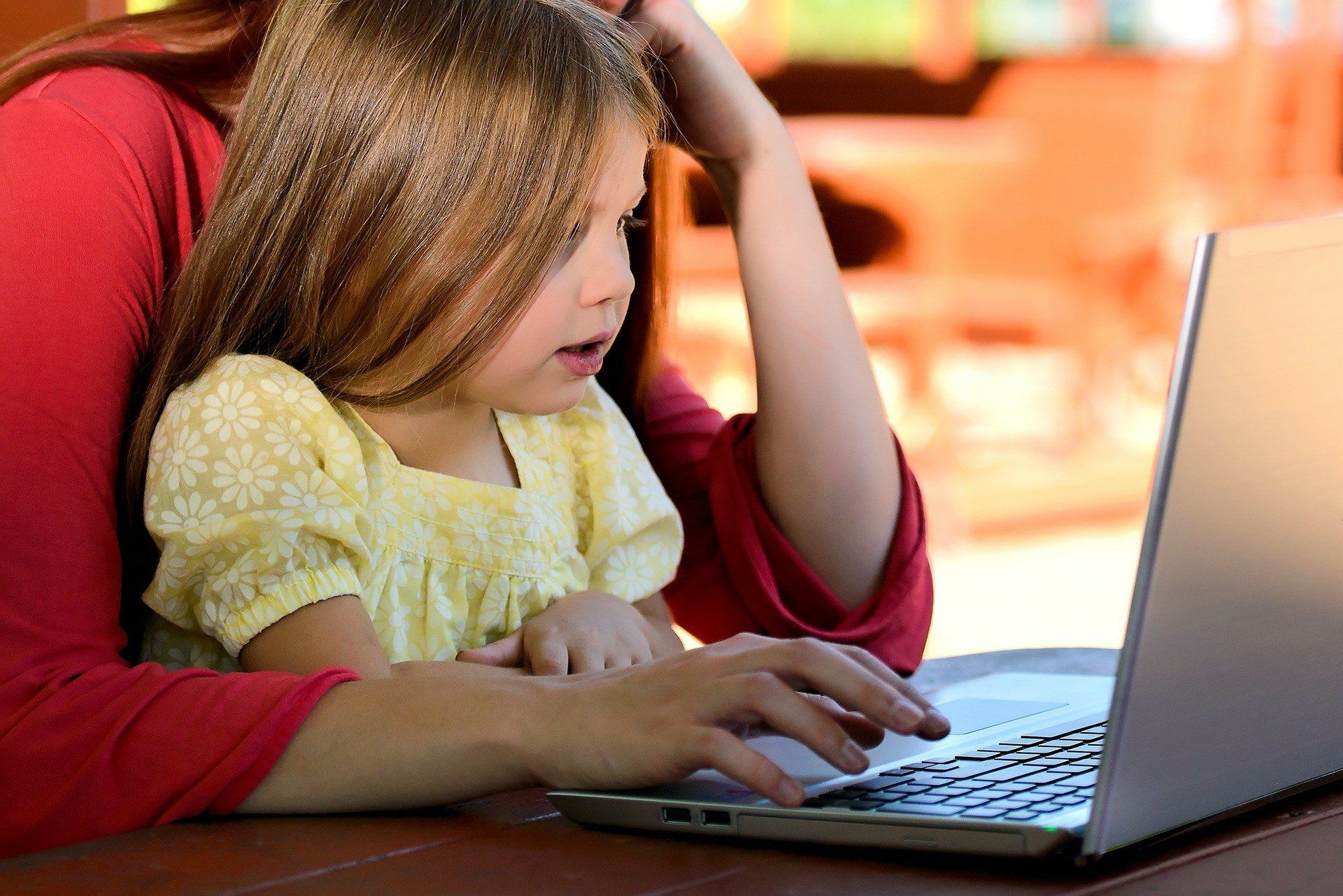 Woman and child looking at a laptop together, in a brightly lit setting.