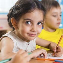 Little Girl Smiling and Doing Homework at Daycare | Goffstown, NH | Educare Daycare & Learning Center Little Girl Smiling and Doing Homework at Daycare | Goffstown, NH | Educare Daycare & Learning Center