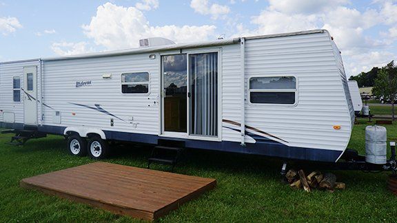 A white trailer is parked in a grassy field next to a wooden platform.
