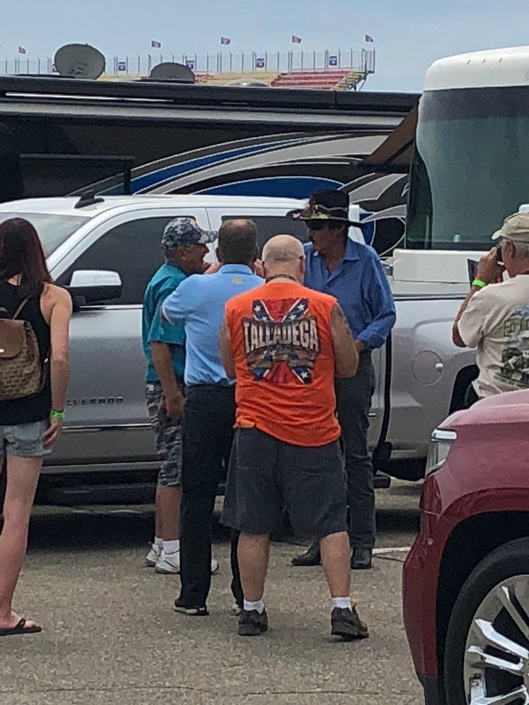 A group of people are standing in a parking lot talking to each other.