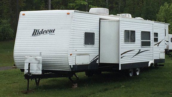 A hideout trailer is parked next to another trailer in a grassy field.