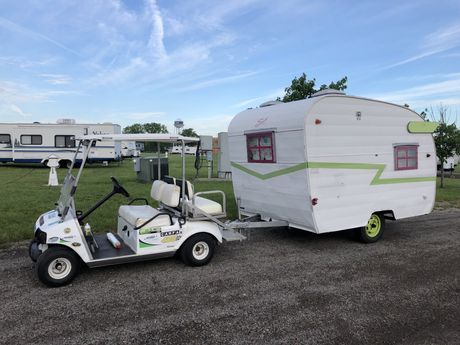 A golf cart is pulling a Shasta trailer