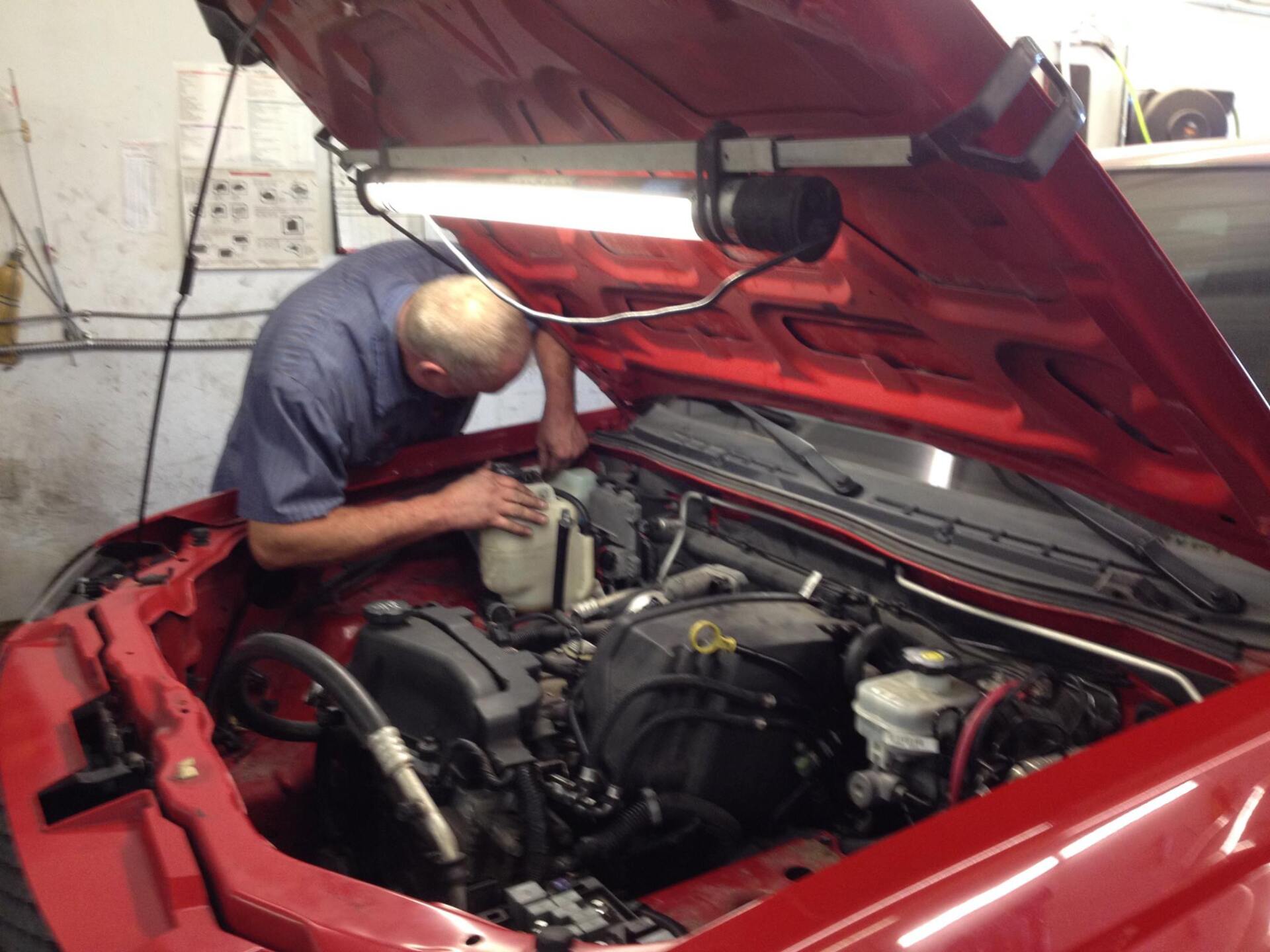 A man is working under the hood of a red car