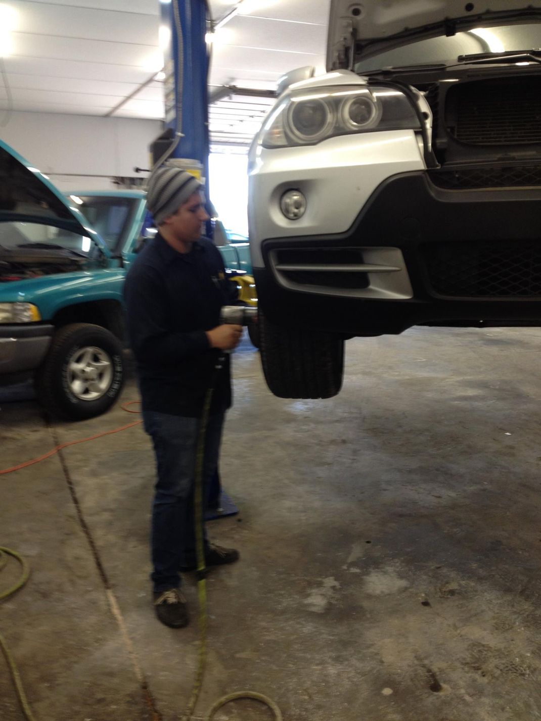 A man is standing next to a car with the hood up in a garage.