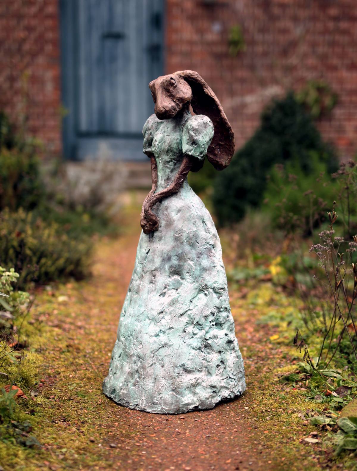 Een standbeeld van een vrouw in een witte jurk met een paraplu in een tuin.