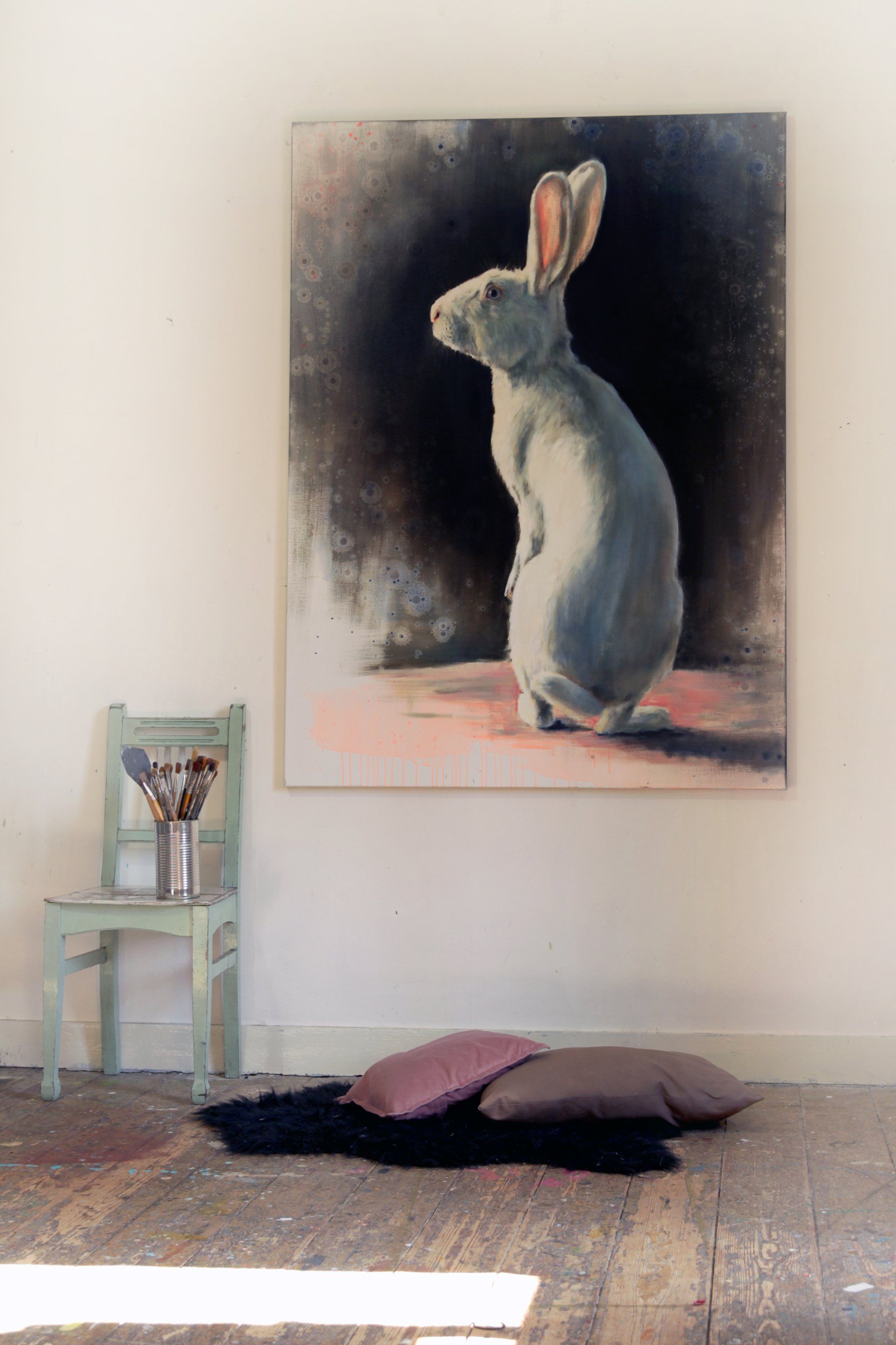 Een schilderij van een konijn hangt aan de muur naast een stoel.
